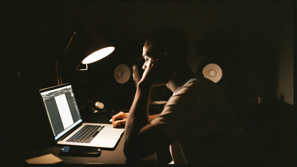 Independent artist working late at a home studio desk, reviewing an invoice on a laptop