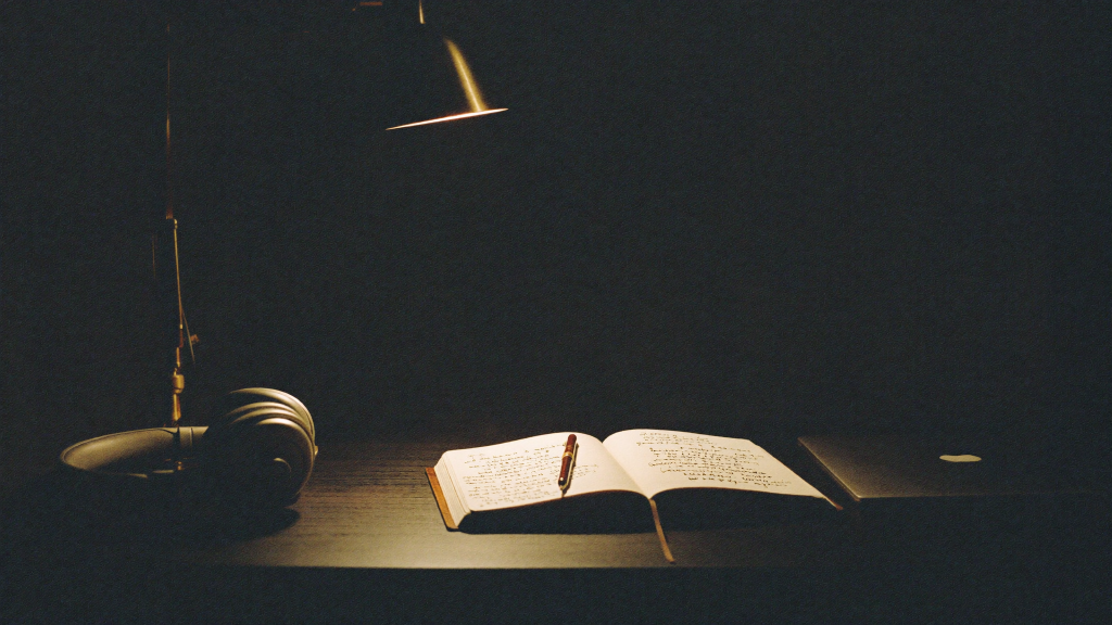 Studio desk with an open notebook, pen, headphones and laptop lit by a warm lamp