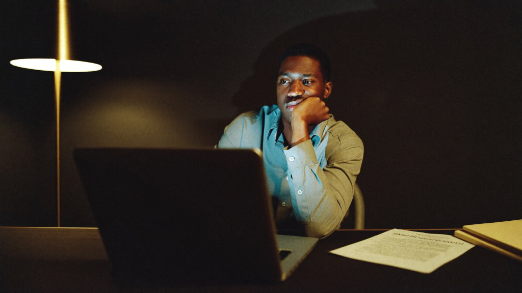 Independent artist studying a laptop and a printed royalty statement late at night