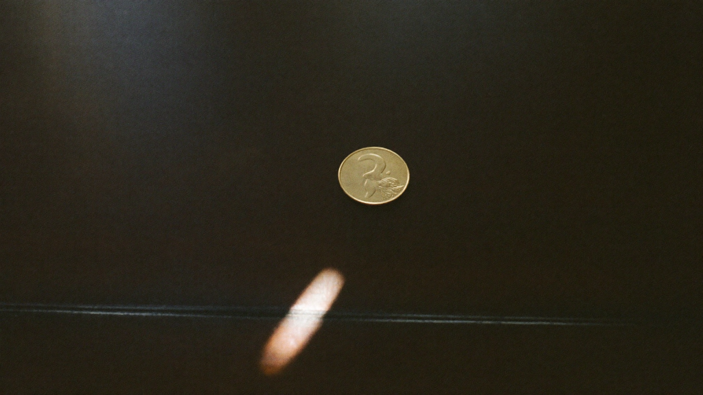A single small coin lit by a narrow beam of light on a vast dark desk