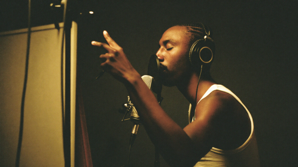 Independent artist wearing studio headphones recording a vocal take at a microphone