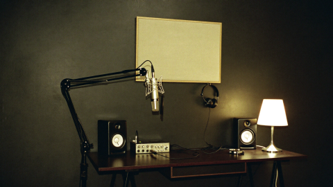Home studio corner with a microphone on a boom arm, audio interface, monitors, headphones and an acoustic panel