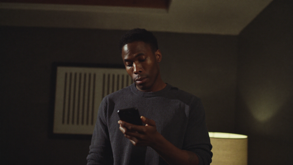 Independent artist standing in a home studio looking thoughtfully at his phone