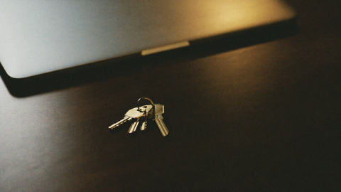 A set of brass keys resting on a dark desk beside a closed laptop under warm light